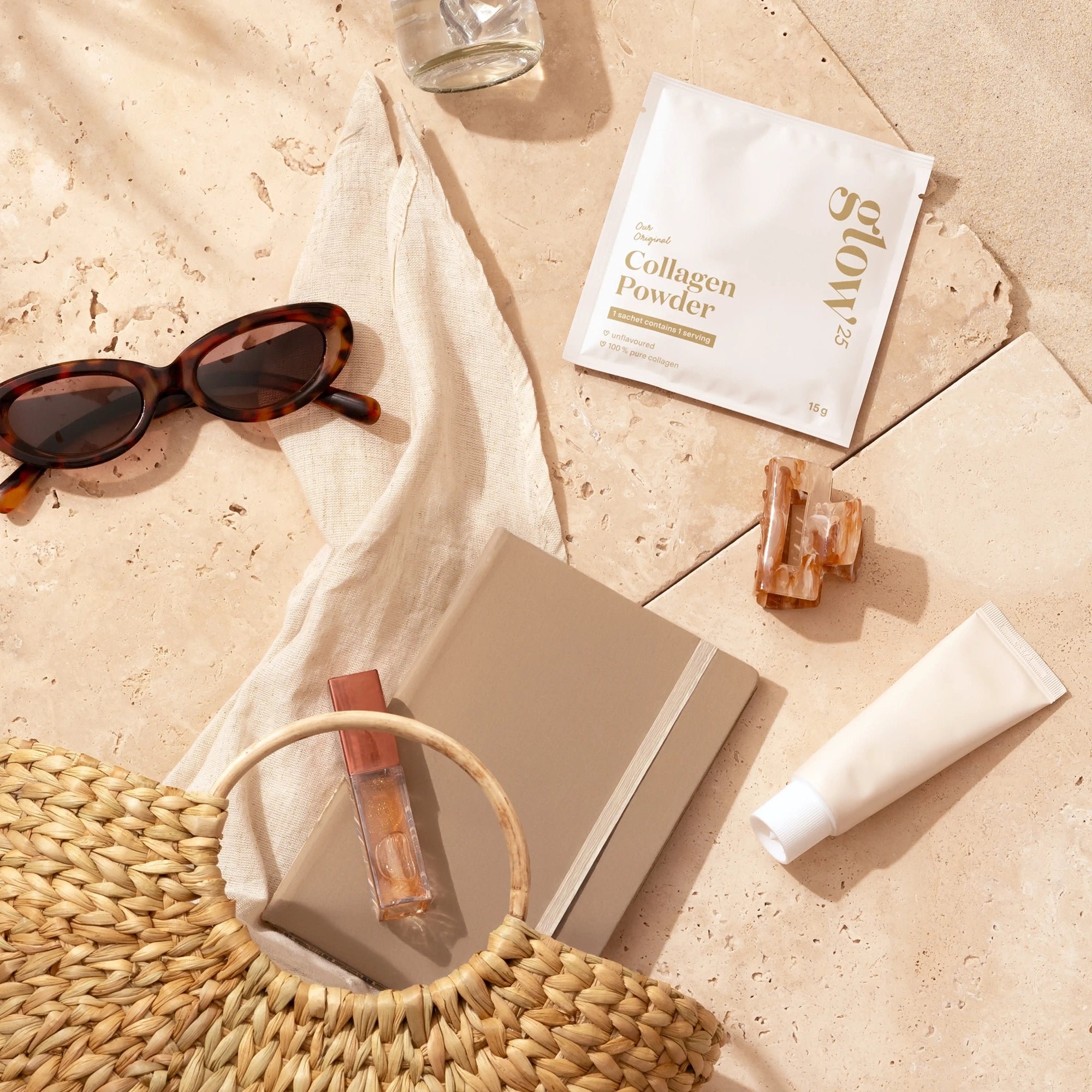 Lifestylebeeld van Glow25 collageen op een stranddoek met zonnebril, notitieboekje en waterglas, symbool voor gezonde routines tijdens de vakantie.