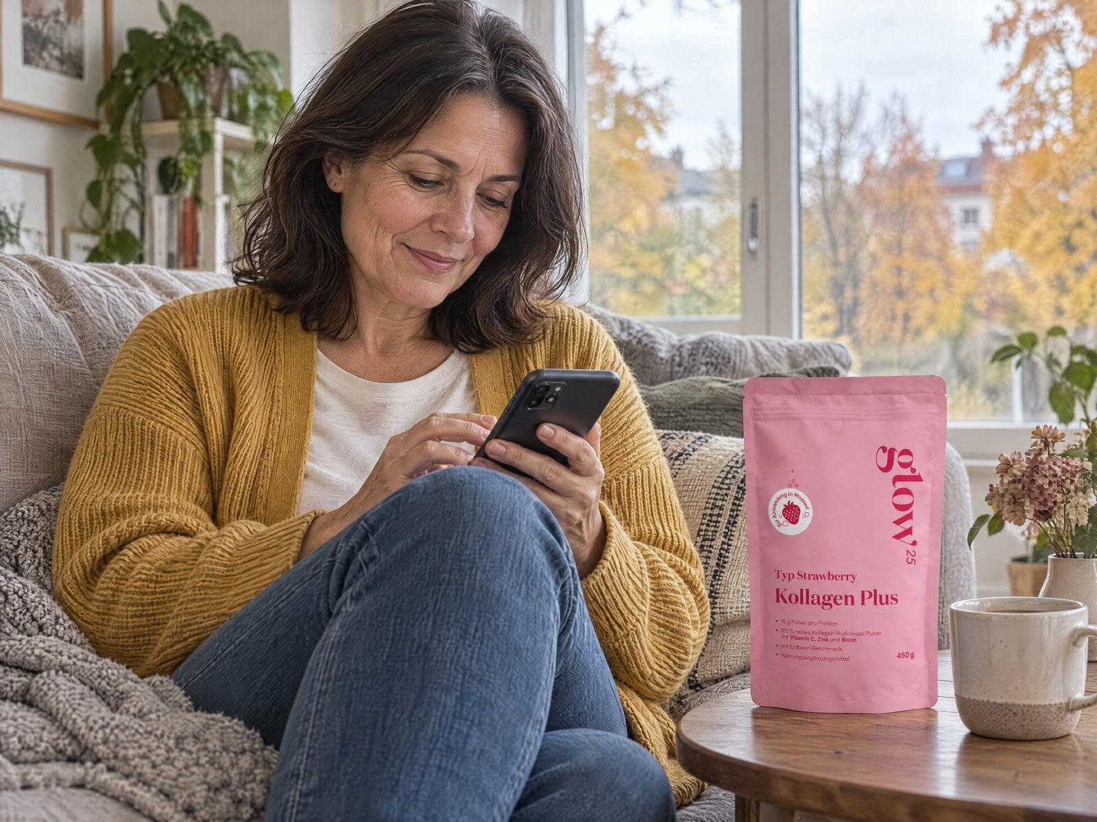 Femme en cardigan moutarde choisissant sur son téléphone, sur le canapé, sa prochaine livraison, à côté Collagène Plus Strawberry