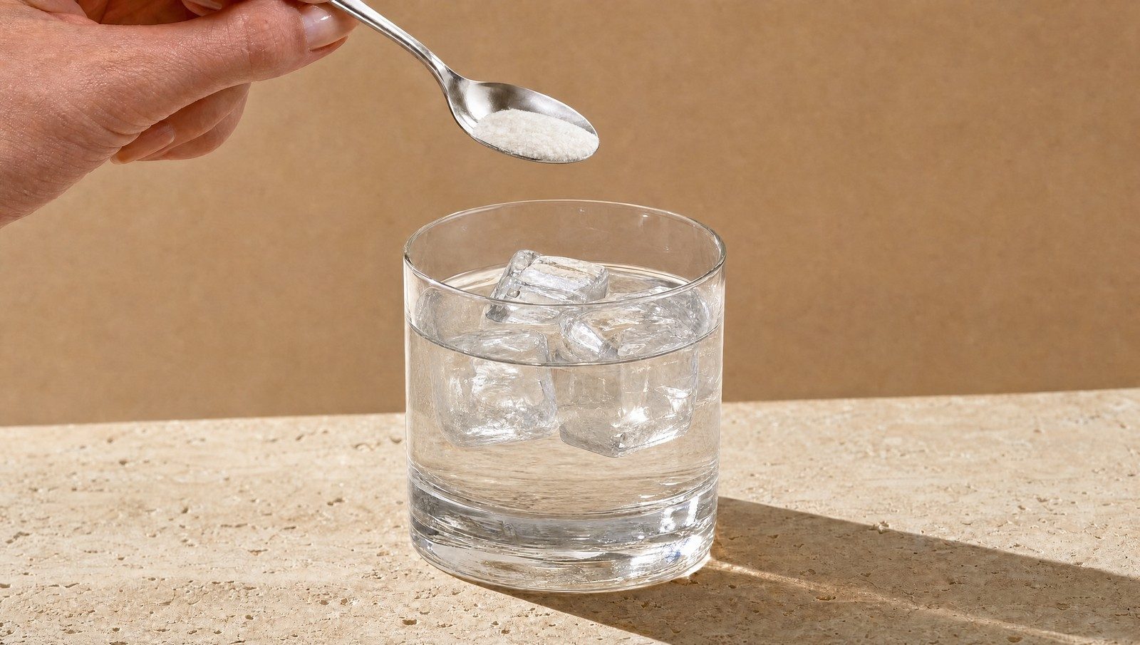 Une cuillère à café verse une poudre blanche dans un verre d'eau avec des glaçons